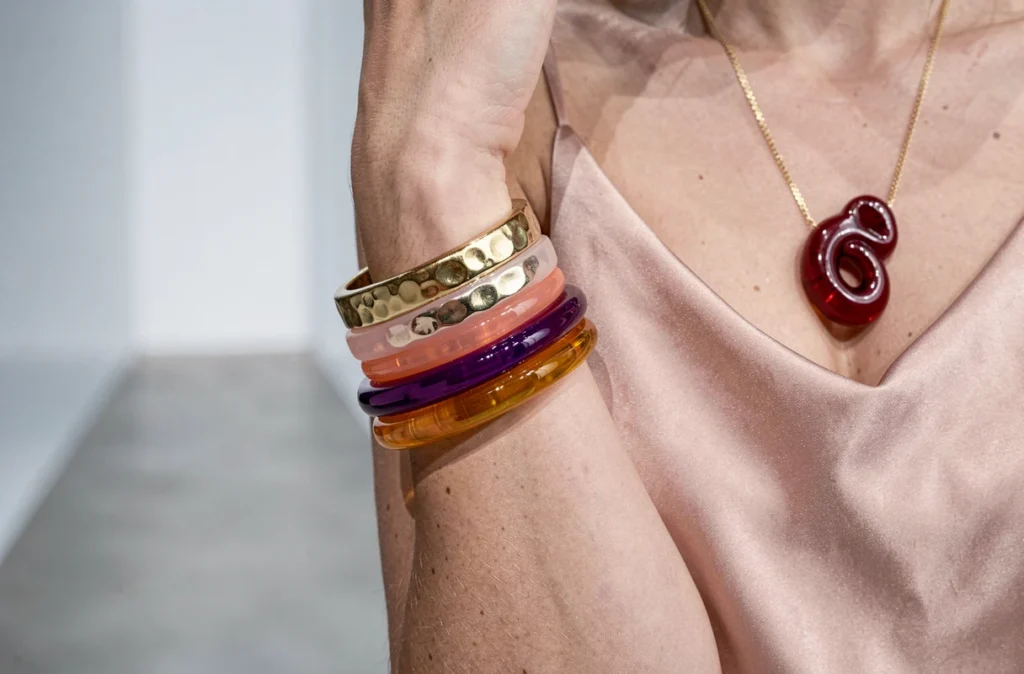 Gros plan sur des bracelets empilés en acrylique coloré et manchette dorée avec collier pendentif rouge rubis sur robe en soie, tendance bijoux de saison
